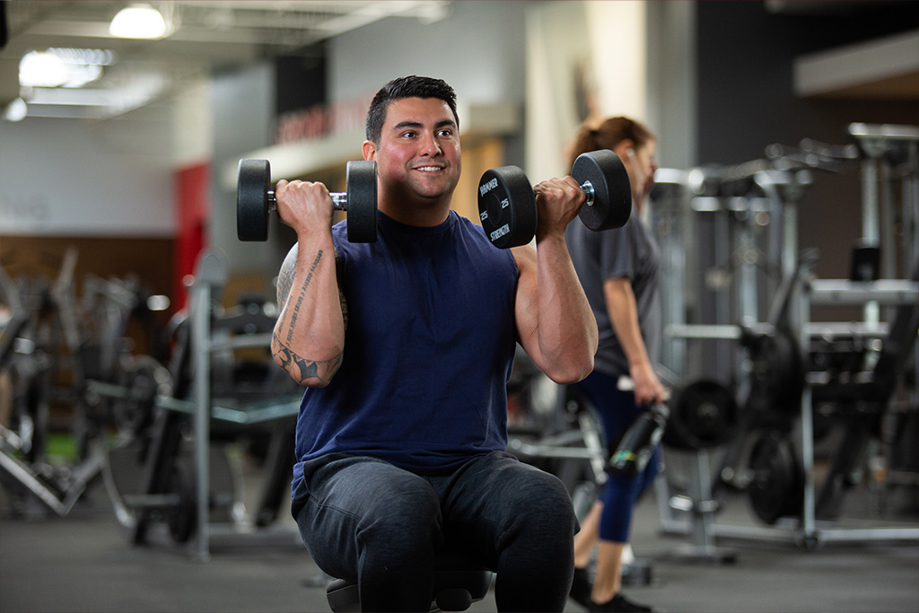 man sitting down doing shoulder presses with dumbbells at a Vasa Gym