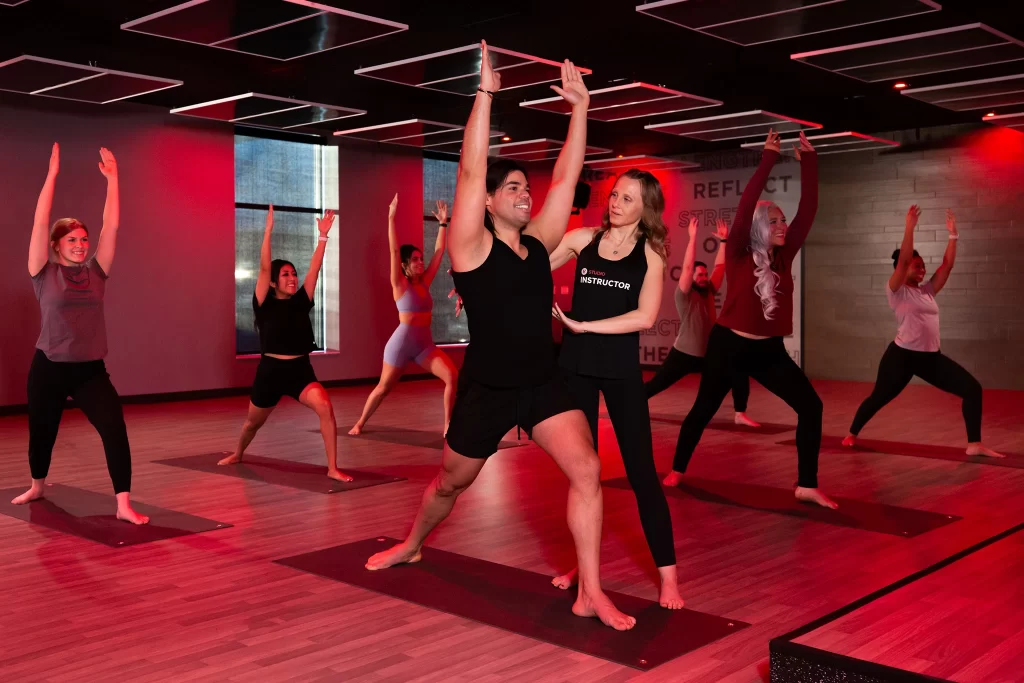 A trainer helping a male athlete stretch in a group yoga STUDIO Flow class in VASA Fitness