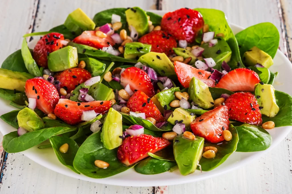 A plate of strawberries mixed with an assortment of fruits and vegetables.